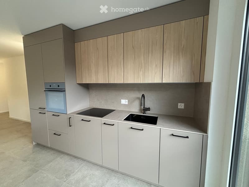 Modern kitchen with light wood cabinets, stainless steel sink, and built-in oven.