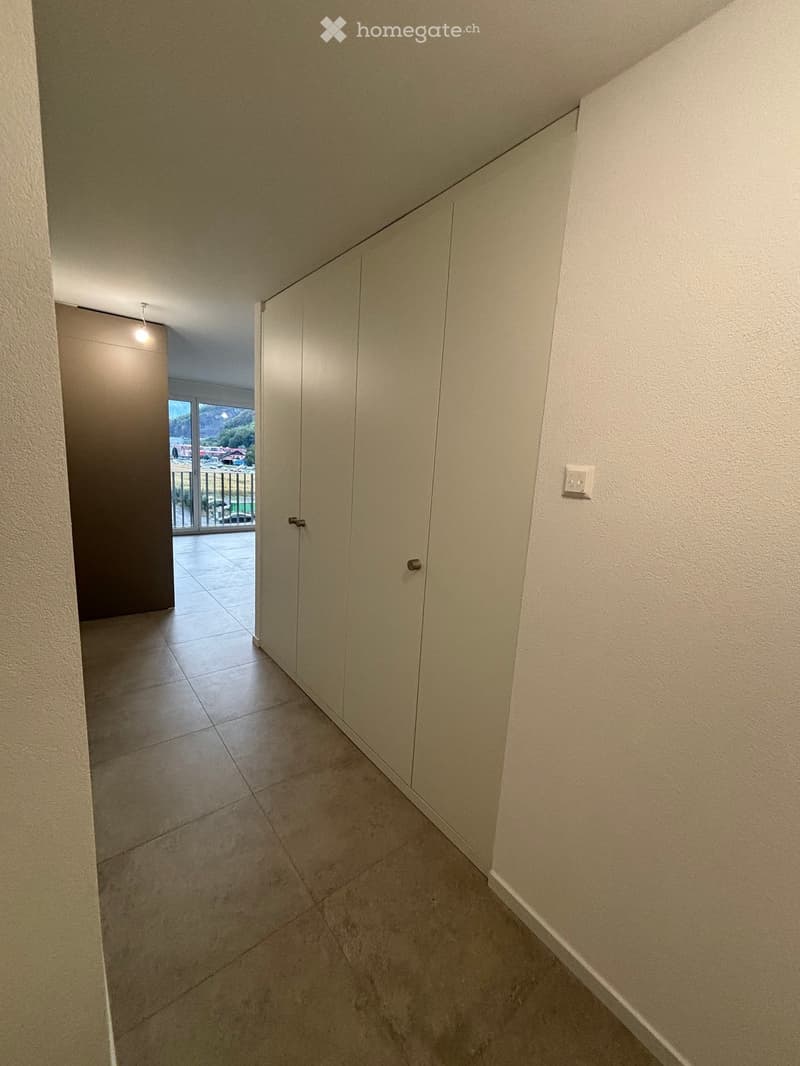 Empty hallway with tiled floor, white walls, and a closed door leading to a balcony area with outdoor view.