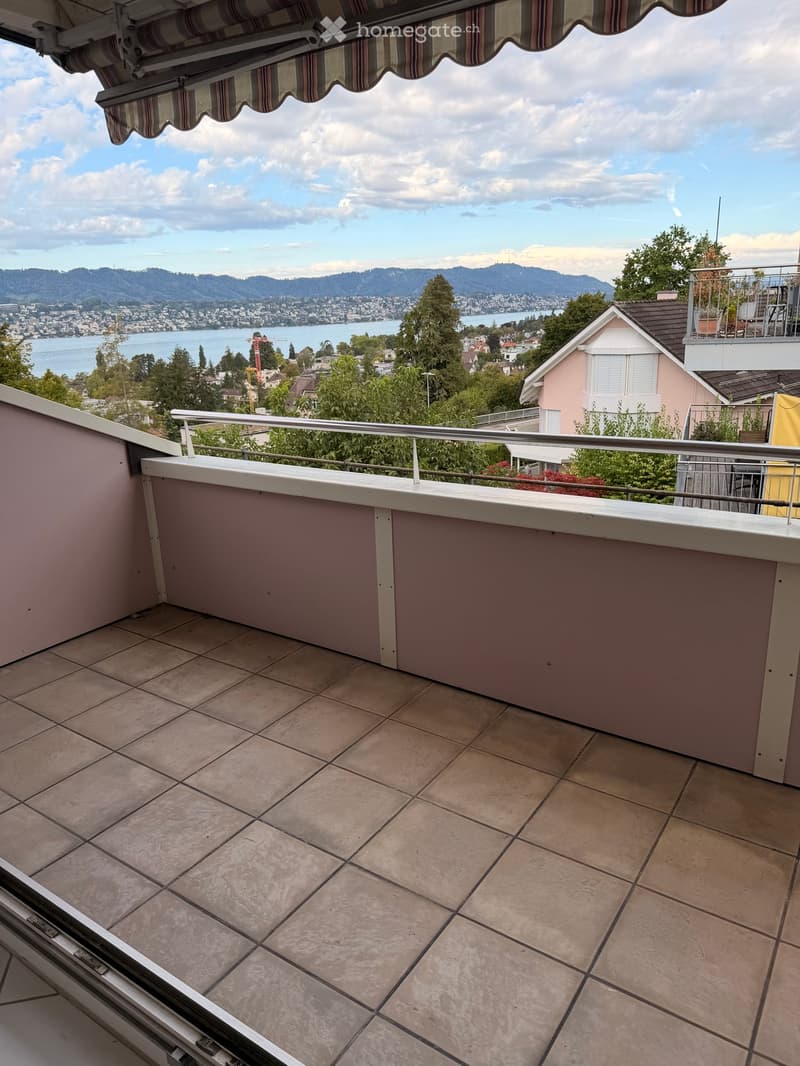 Balcony with tiled floor, metal railing, and scenic view of a lake and mountains.