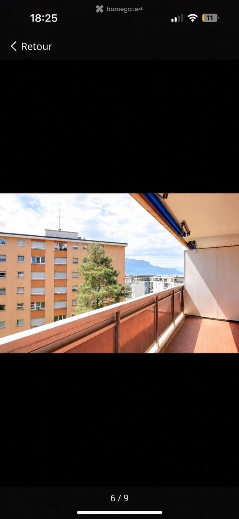 Balcony with wooden flooring, metal railing, and a view of a tree, building, and mountains.