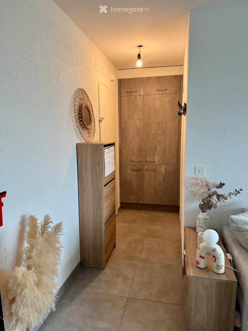 Modern hallway with tiled floor, wooden cabinetry, decorative wall pieces, and a small side table with a vase and decorative items.