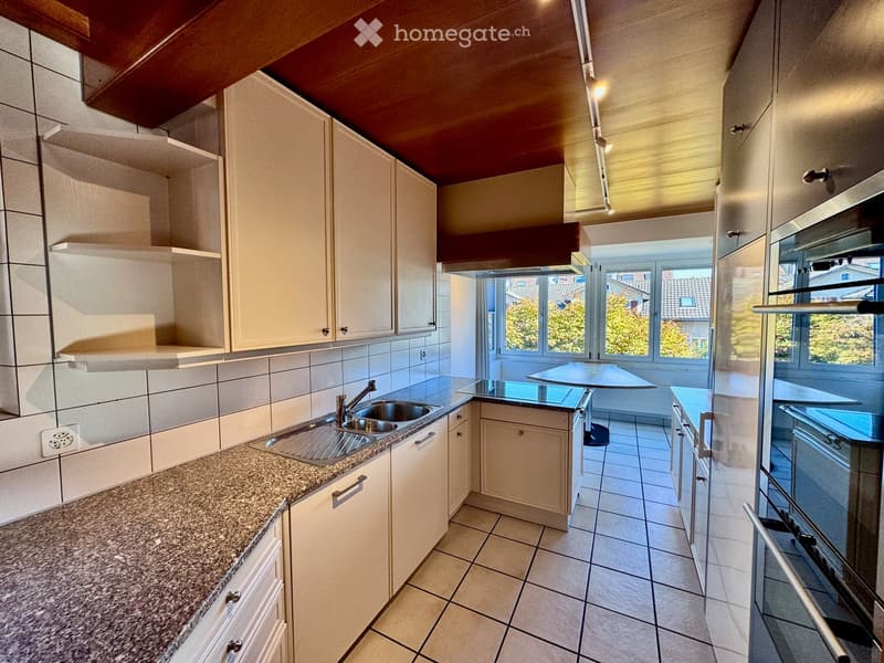 Modern kitchen with white cabinets, granite countertop, stainless steel sink, and large windows overlooking a garden.