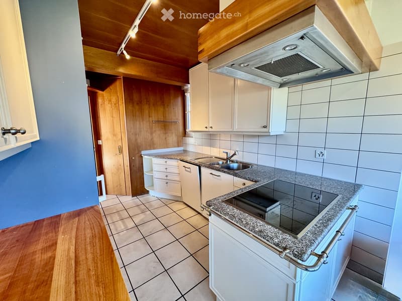 Modern kitchen with granite countertops, white cabinets, stainless steel sink, and range hood. Wooden flooring and tiled backsplash.