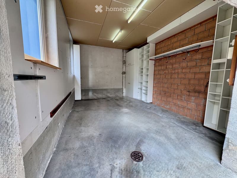Empty room with concrete floor, exposed brick wall, built-in white shelving units, and a coat rack with hooks.