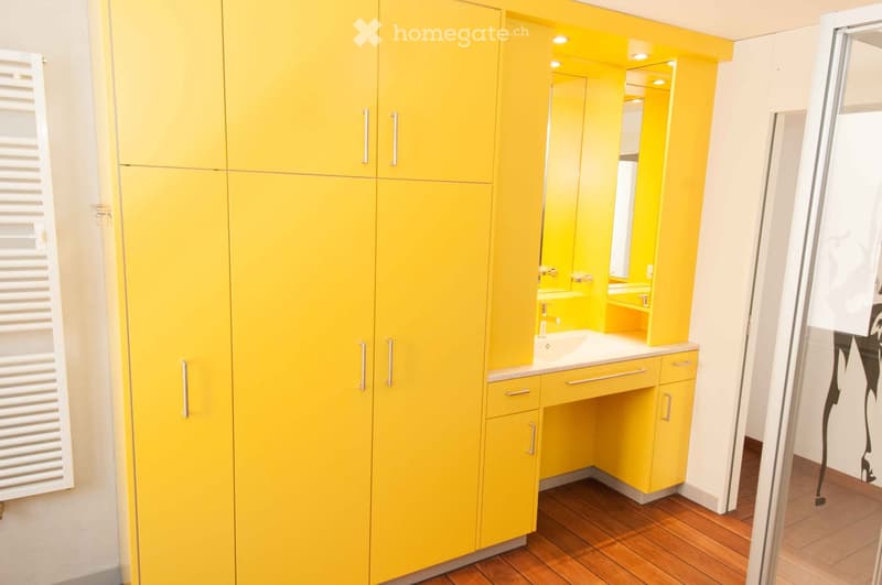 Bright yellow bathroom with modern cabinets, a sink, and a mirror. Wooden flooring and white radiator visible.