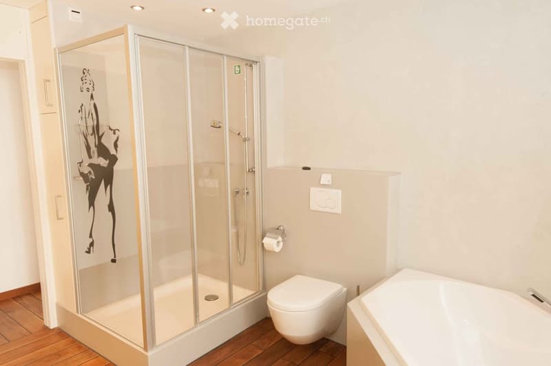 Modern bathroom with a glass-enclosed shower, toilet, bathtub, and wooden flooring.