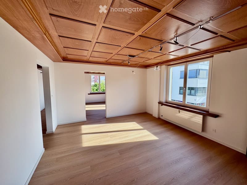 Empty room with wooden flooring, white walls, and a wooden ceiling. Features include large windows, recessed lighting, and a radiator under one window.