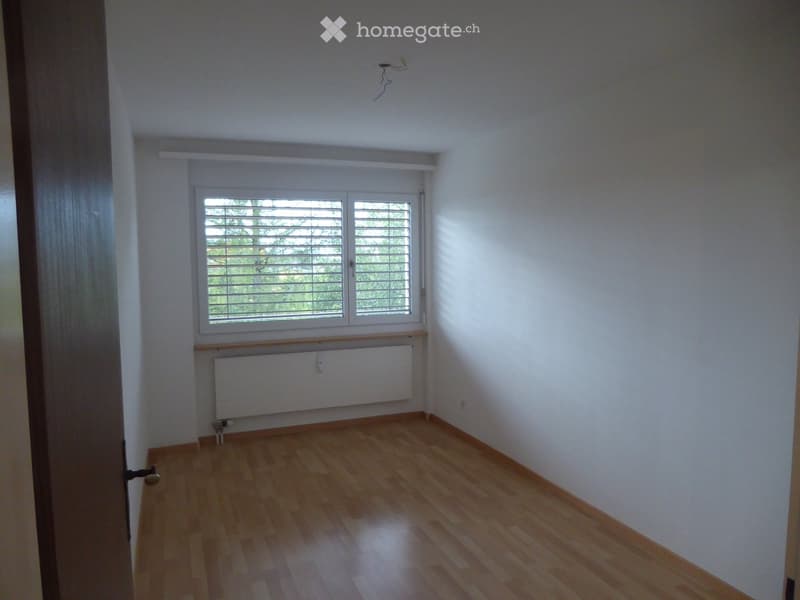 Empty room with wooden flooring, white walls, a window with blinds, and a radiator below the window.
