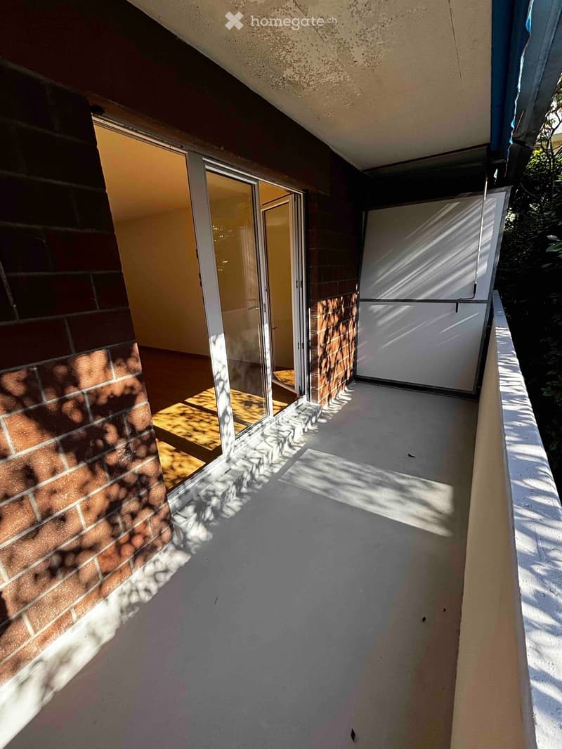 Balcony with glass sliding doors, brick walls, and a concrete floor.