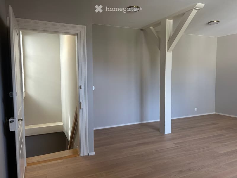 Empty room with wooden flooring, white walls, and a partially visible adjacent room through an open doorway.