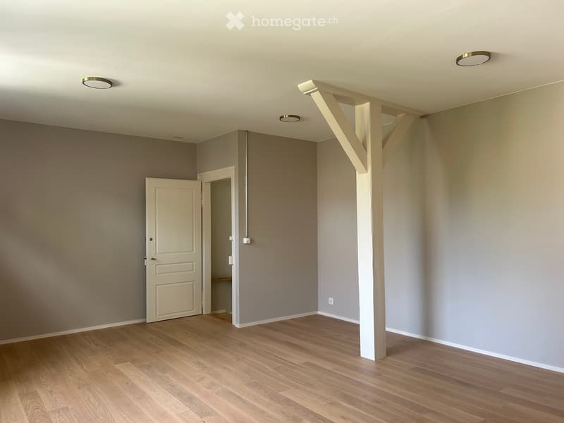 Empty room with wooden flooring, neutral-colored walls, and recessed lighting. Features an open doorway leading to another space.