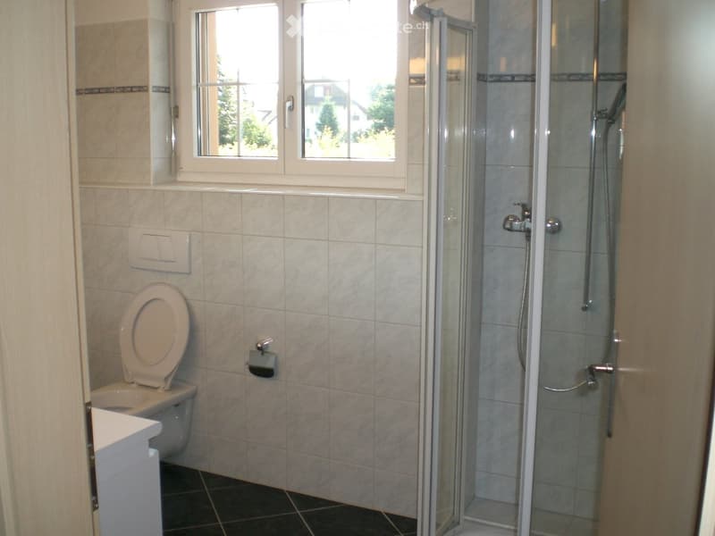Bathroom with a toilet, a glass-enclosed shower, and a window offering a view of the outside.
