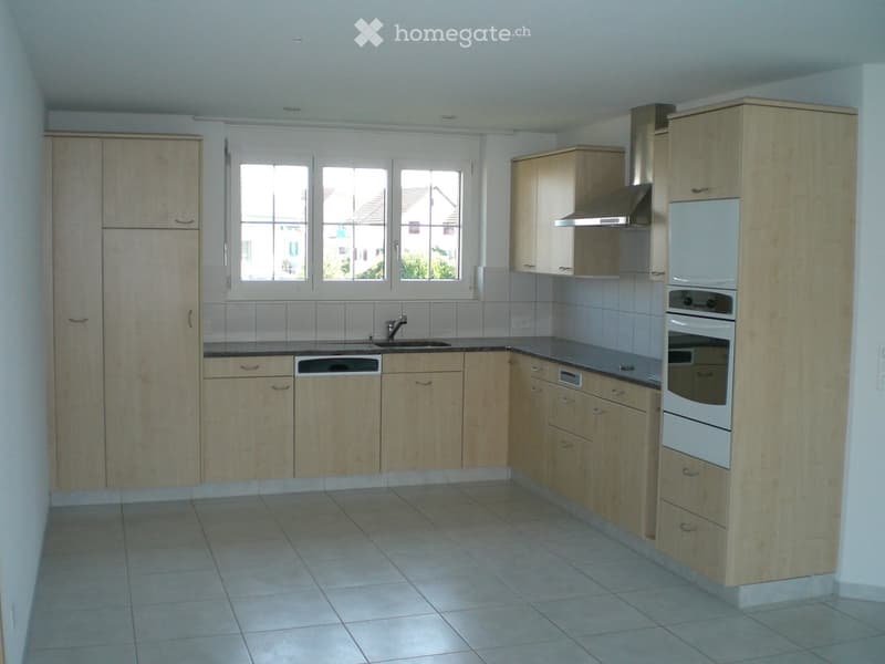Modern kitchen with light wooden cabinets, tiled floor, and stainless steel appliances including a sink, dishwasher, and oven.