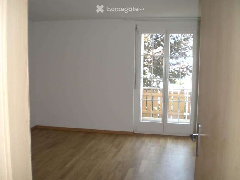 Empty room with wooden flooring and white walls, featuring a large sliding glass door with a view of an outdoor area.