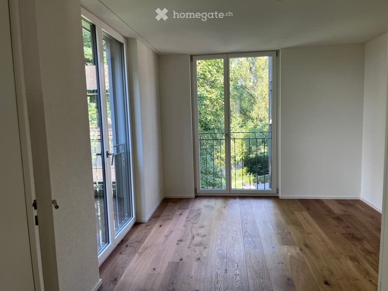 Empty room with wooden flooring, large windows, and sliding glass doors leading to a balcony.
