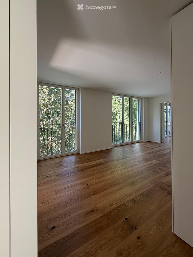 Empty room with wooden flooring, large windows, and a view of greenery outside. No furniture or equipment present.