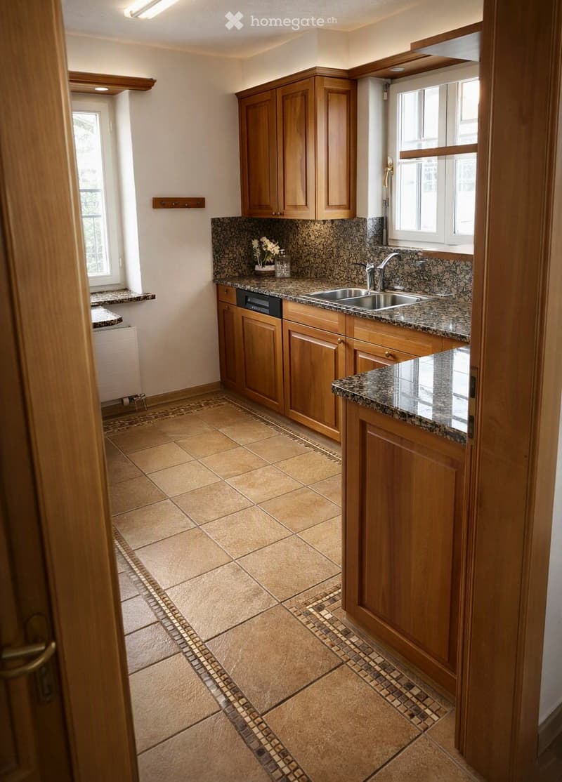 Modern kitchen with wooden cabinets, granite countertops, and a stainless steel sink. The floor is tiled with a decorative border.