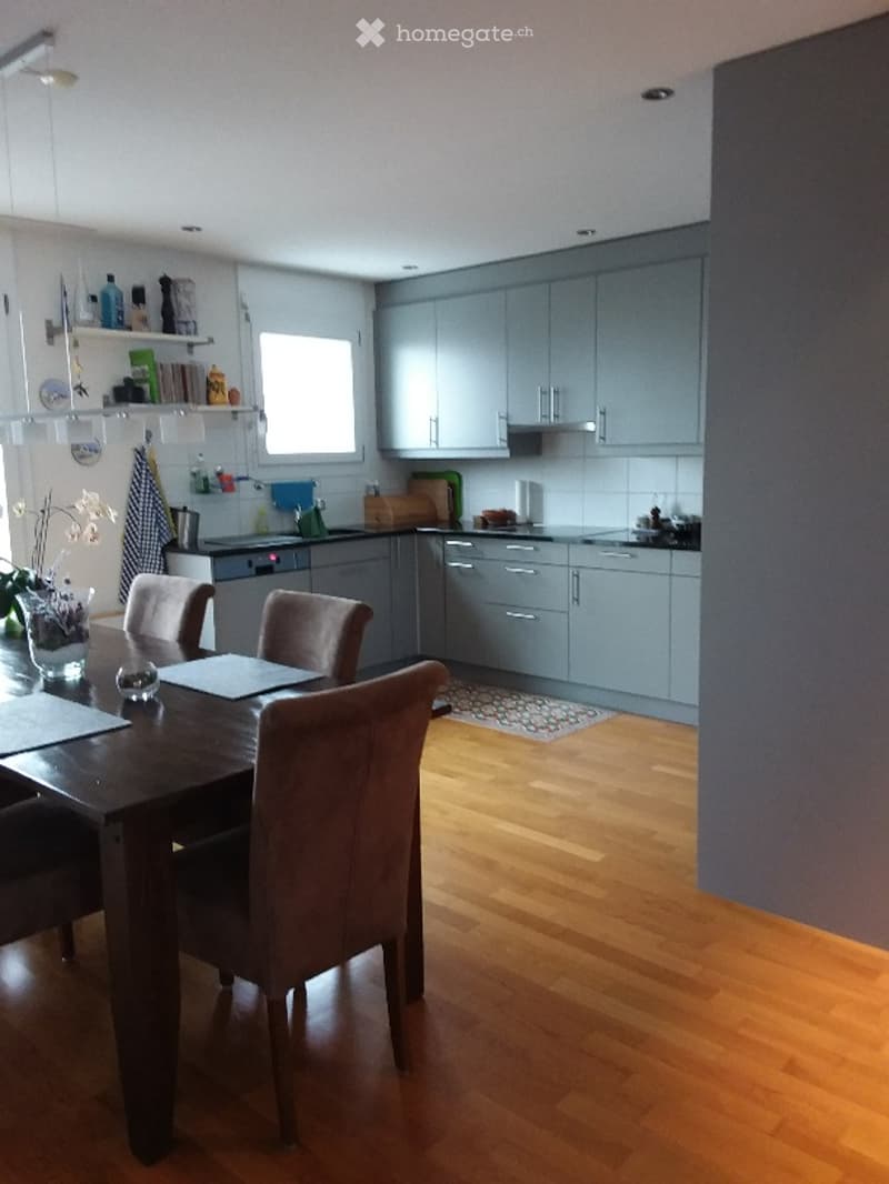 Modern kitchen and dining area with grey cabinets, wooden flooring, a dining table with chairs, and various kitchen appliances.