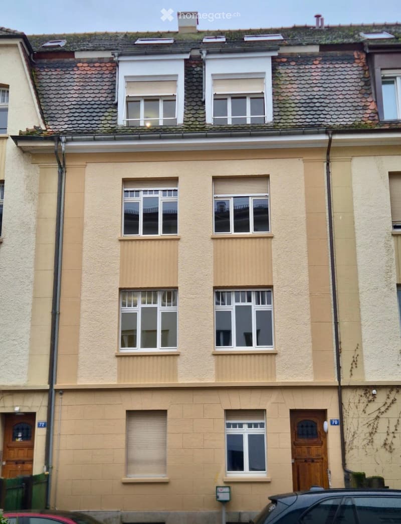 Two-story residential building with beige facade, multiple windows with shutters, and wooden doors.