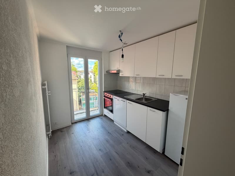 Modern kitchen with white cabinets, a black countertop, a sink, an oven, and a refrigerator. The space features wooden flooring and large windows with a view of the outside.