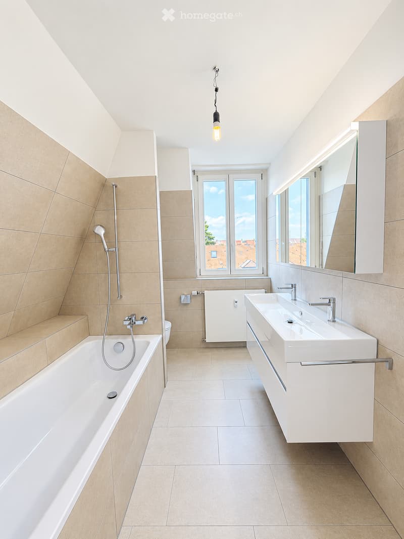 Modern bathroom with a bathtub, double sink, large mirror, and a window offering a view of the city.