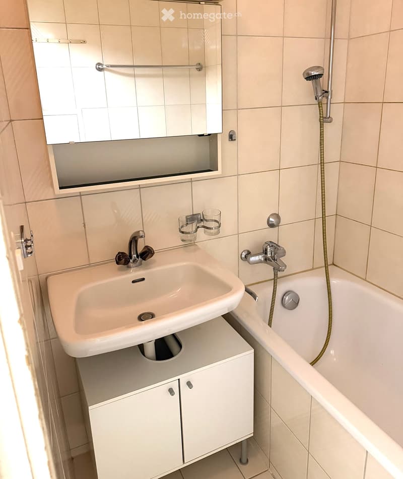 Modern bathroom with a white sink, bathtub, mirror, and cabinet.