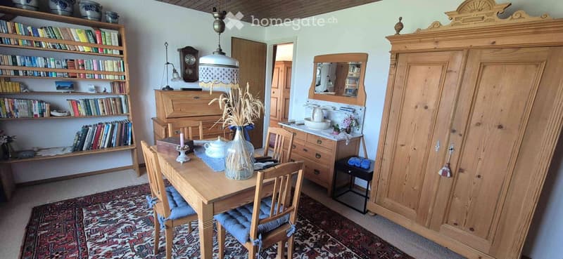 Cozy dining area with wooden table, chairs, bookshelf, and antique furniture.