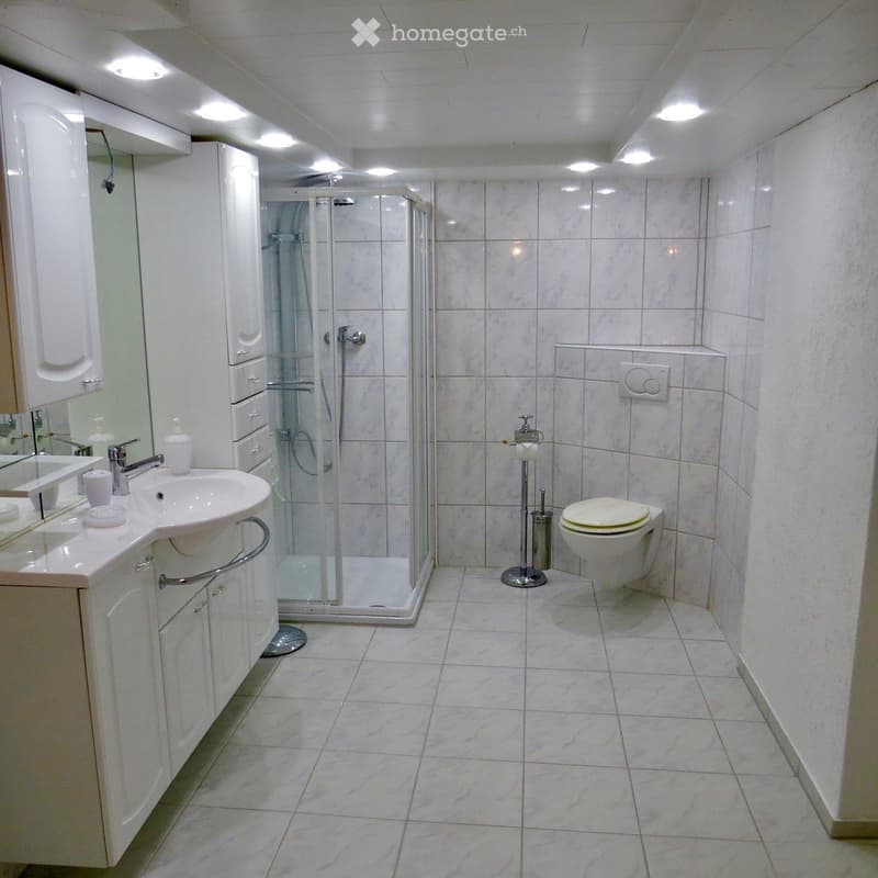 white tiled floor, white tiled walls, glass shower enclosure, white sink, white toilet, white cabinets, mirror
