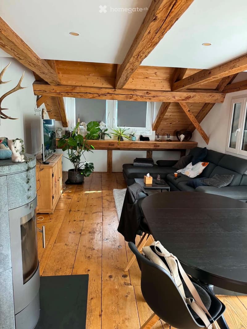 A modern living room with wooden beams, hardwood floors, a grey sectional sofa, a coffee table, a dining table with chairs, and a fireplace.
