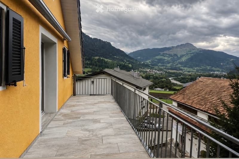 Balcony with tiled flooring, metal railing, overlooking a scenic mountain landscape and valley below.