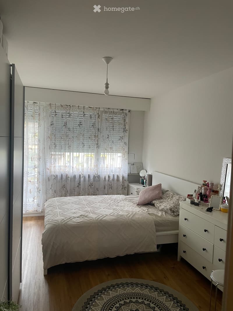 Cozy bedroom with a single bed, patterned quilt, pink pillow, nightstand, mirror, and a small round rug on the floor.