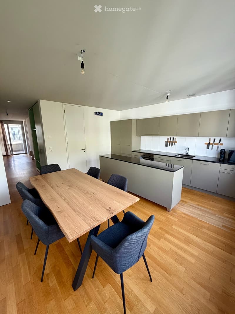 Modern kitchen with light grey cabinets, a wooden dining table with four chairs, and a sleek kitchen island with built-in appliances.