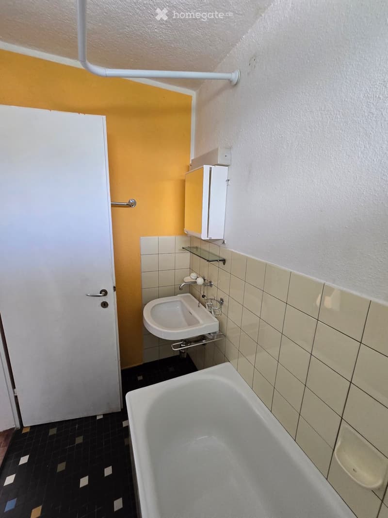 Bathroom with a bathtub, sink, mirror, and cabinet. The walls are tiled, and the floor is covered with dark tiles.