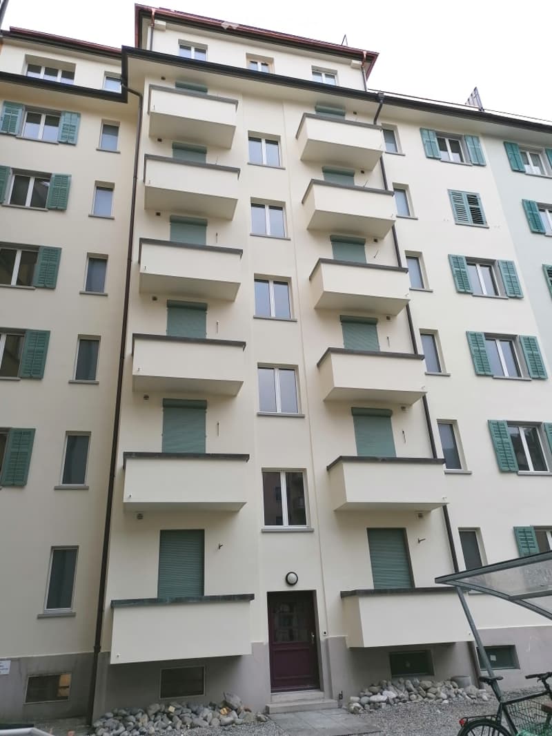 Multi-story residential building with multiple balconies, green shutters, and a central entrance.