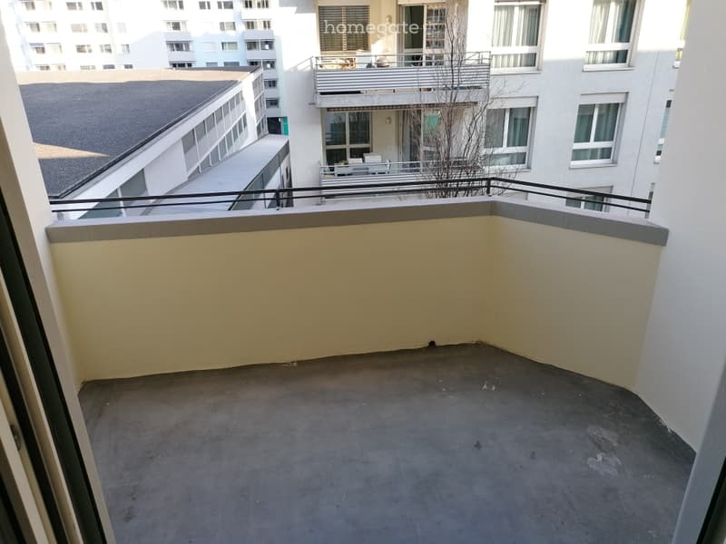 Empty balcony with concrete floor, metal railing, and view of neighboring buildings.