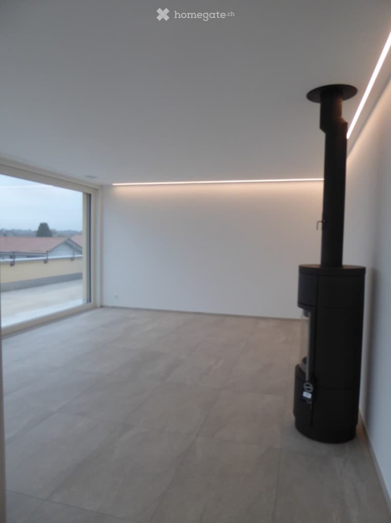 Empty room with tiled floor, white walls, large window, and a black wood-burning stove.