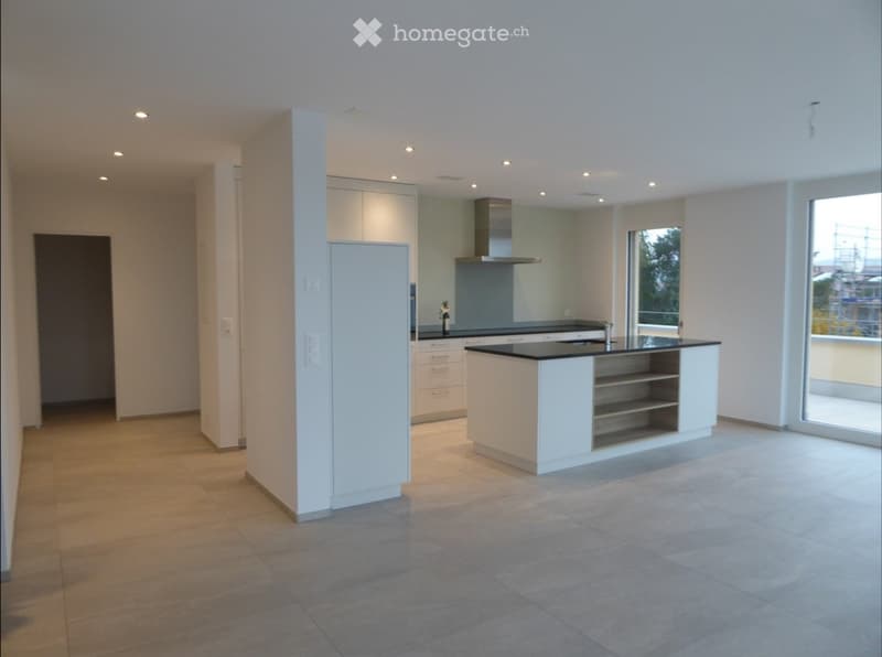 Modern kitchen with white cabinets, a central island, and a black countertop. Features include a range hood, sink, and large windows providing natural light.
