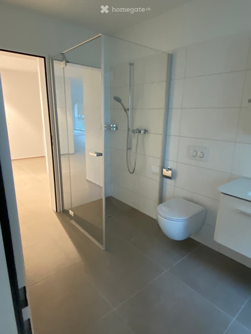 Modern bathroom with a glass-enclosed shower, toilet, and sleek tile flooring.