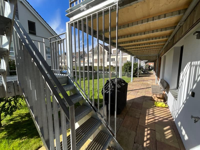 Balcony with metal railings, tiled floor, and steps leading to a grassy area.