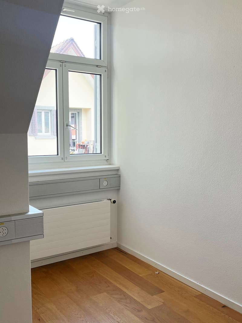 Empty room with wooden flooring, white walls, and a window with a radiator below it.