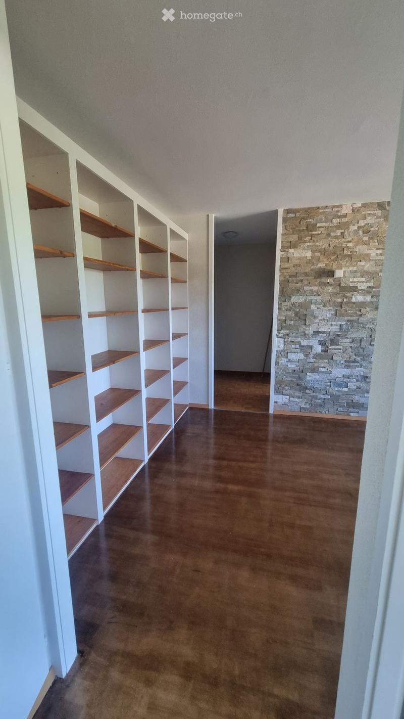 Empty room with wooden flooring, white built-in shelving units with wooden shelves, and a stone accent wall.