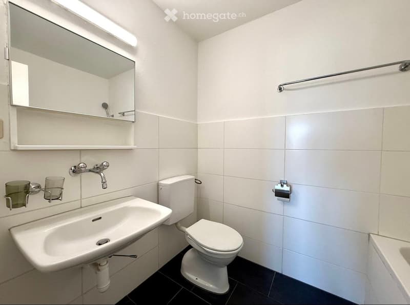 Modern bathroom with white tiles, a sink, toilet, mirror, and towel rack.