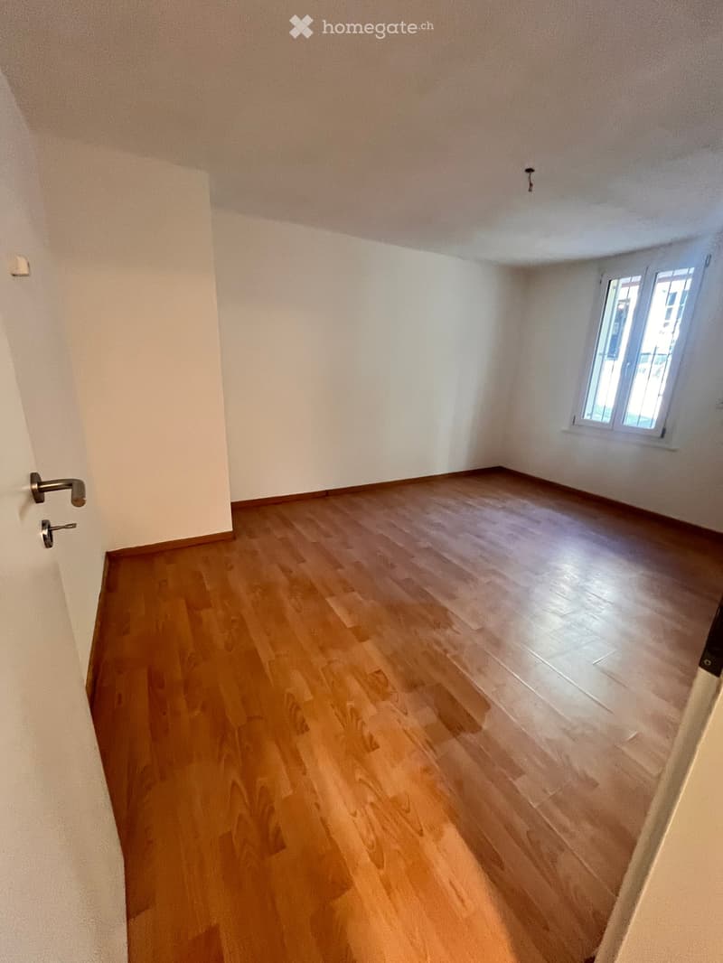 Empty room with wooden flooring and white walls, featuring a window and a door with a handle.