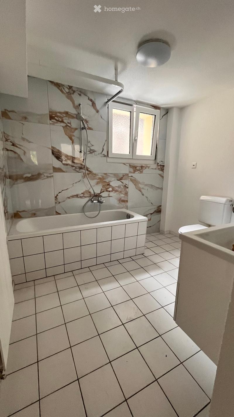 Bathroom with white tiled floor, marble-patterned shower walls, bathtub, toilet, and sink.