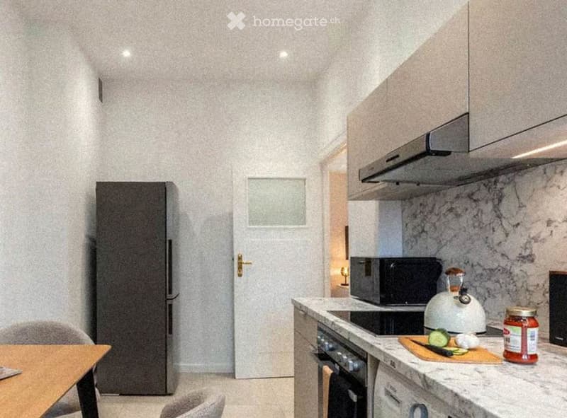Modern kitchen with marble countertops, stainless steel appliances, and a small dining area.