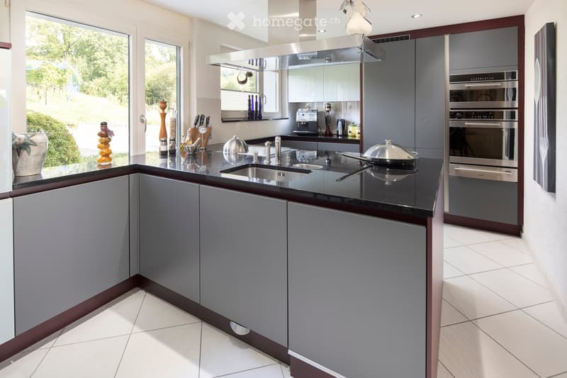 Modern kitchen with grey cabinets, black countertop, stainless steel appliances, and decorative items on the counter.