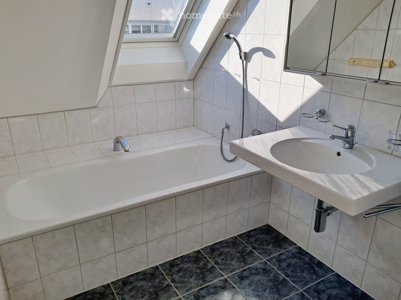 Modern bathroom with a bathtub, sink, and mirror, featuring tiled walls and a skylight window.