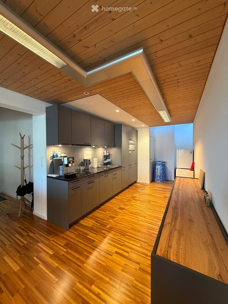 Modern kitchen with grey cabinets, wooden flooring, and stainless steel appliances including a refrigerator, coffee machine, and sink.