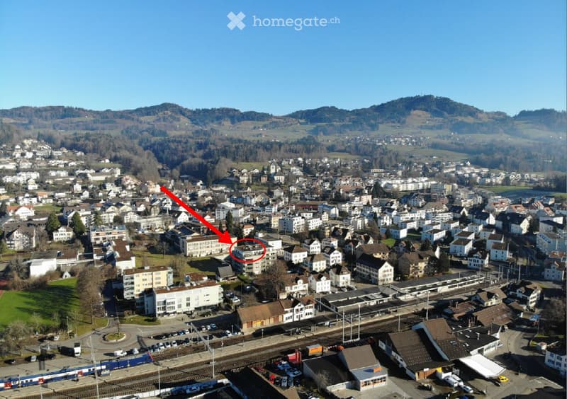 Aerial view of a town with numerous buildings, a train station, and surrounding hills.