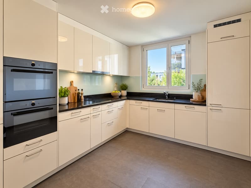 Modern kitchen with white cabinets, black countertops, and stainless steel appliances. Features an oven, sink, and various decorative items on the counter.
